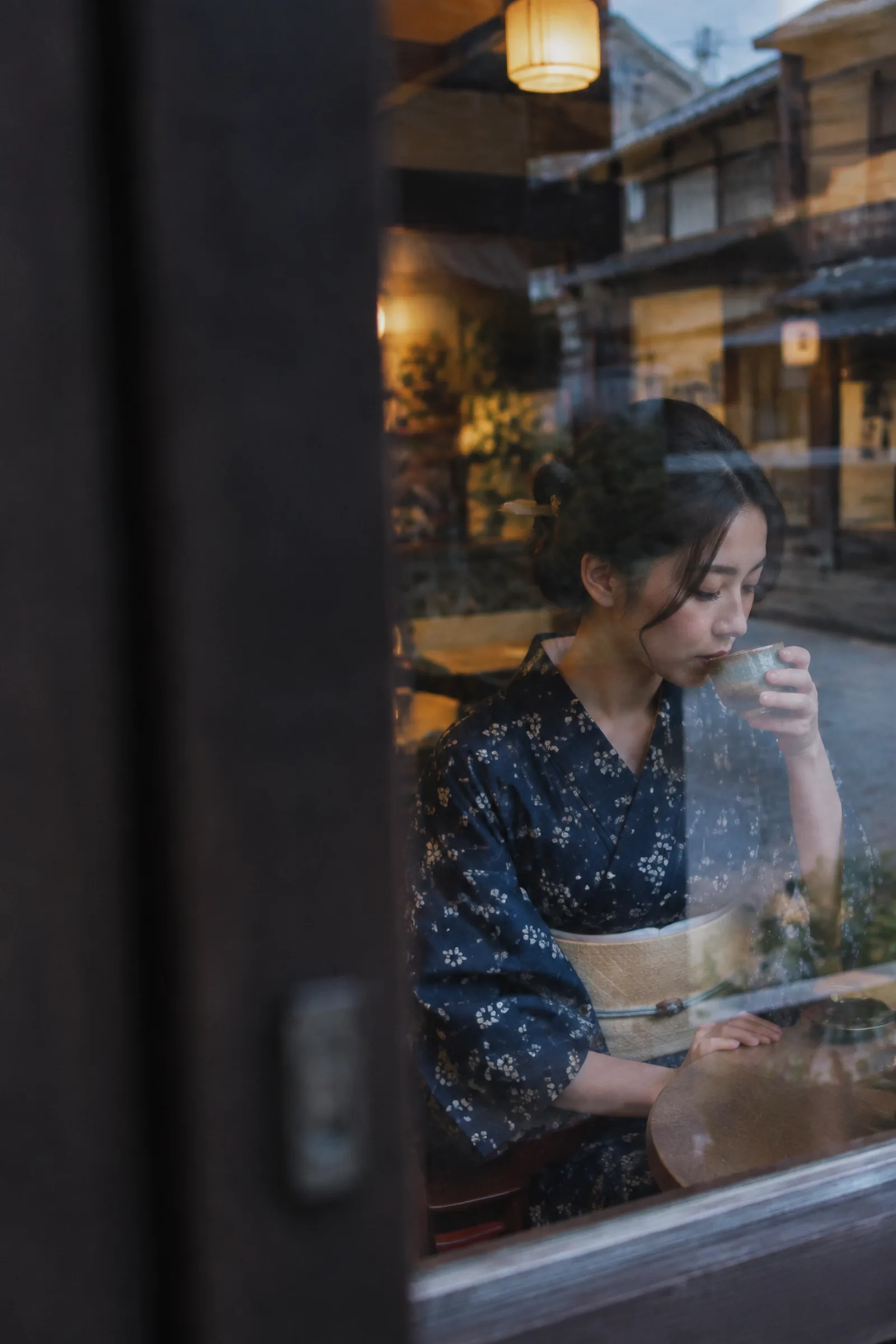 一位约30岁的成年女性，黑发挽起并饰以木质发簪，完整穿着靛蓝细花和服，浅米色腰带